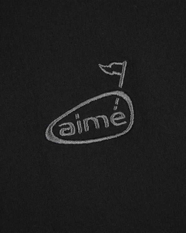 ALD Golf Cordura Tips Jacket: grey aimé logo with flag above the e, embroidered on plain black fabric.