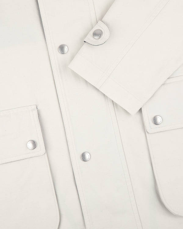 Close-up of the Sailing Jacket in white, with silver snaps, two front pockets, and one sleeve folded across the front.