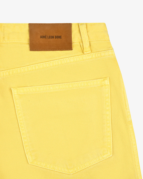 Close-up of yellow Garment Dyed Relaxed Fit Denim pocket with brown Aimé Leon Dore label above the waistband.