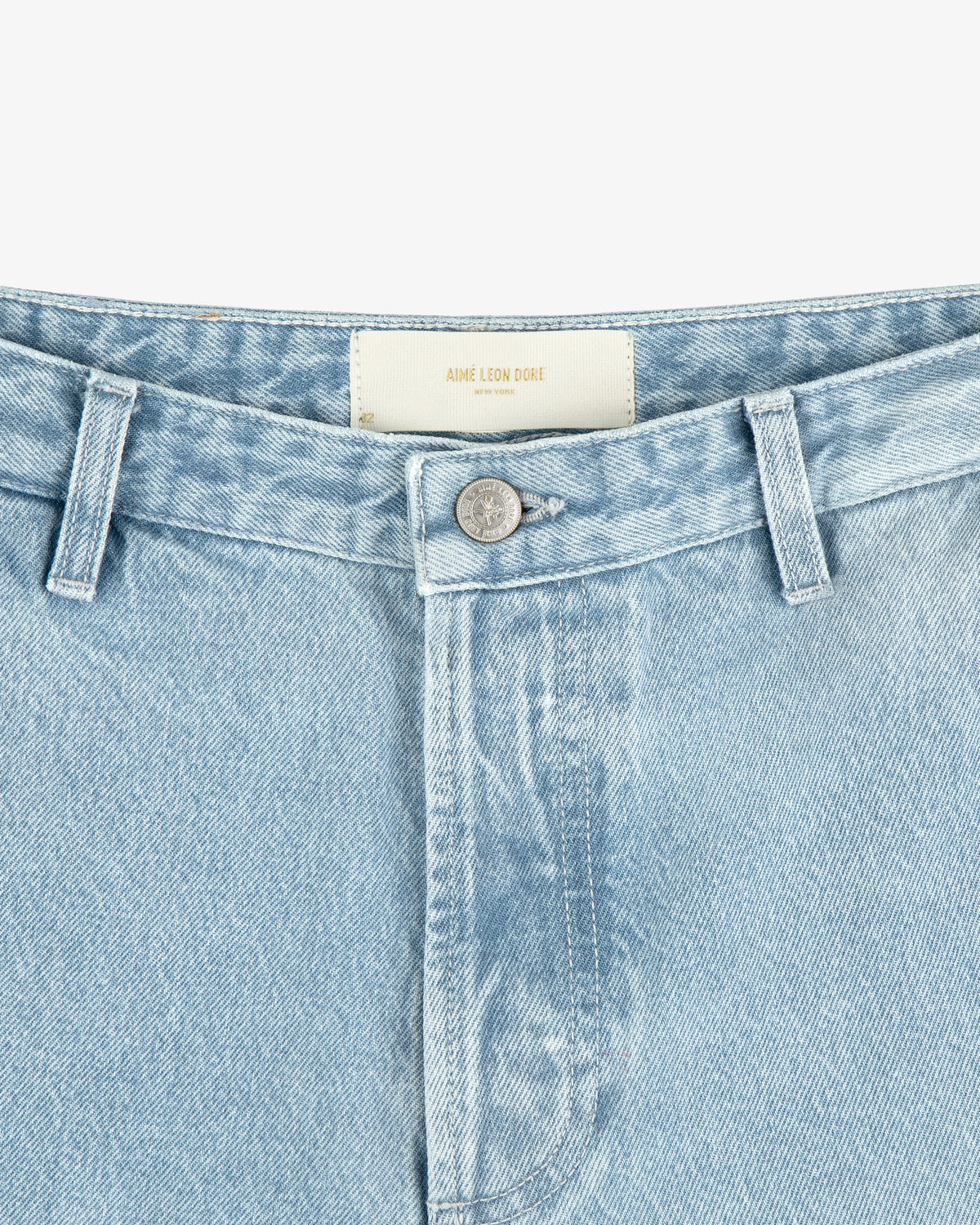 Close-up of Denim Carpenter Pant in light blue wash with a silver button and AIMÉ LEON DORE waistband label.