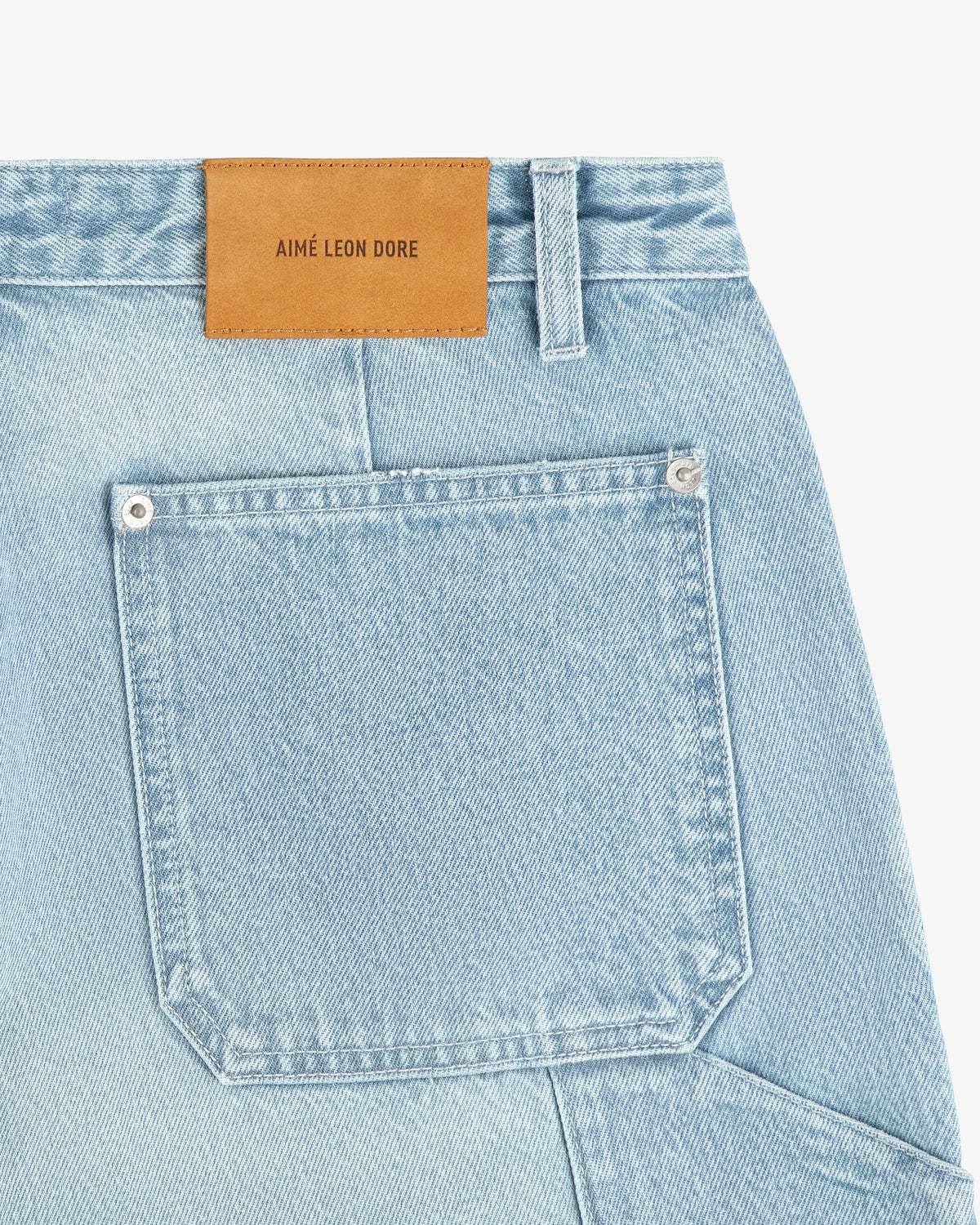 Close-up of light blue Denim Carpenter Pant with a brown leather Aimé Leon Dore label above the back pocket.