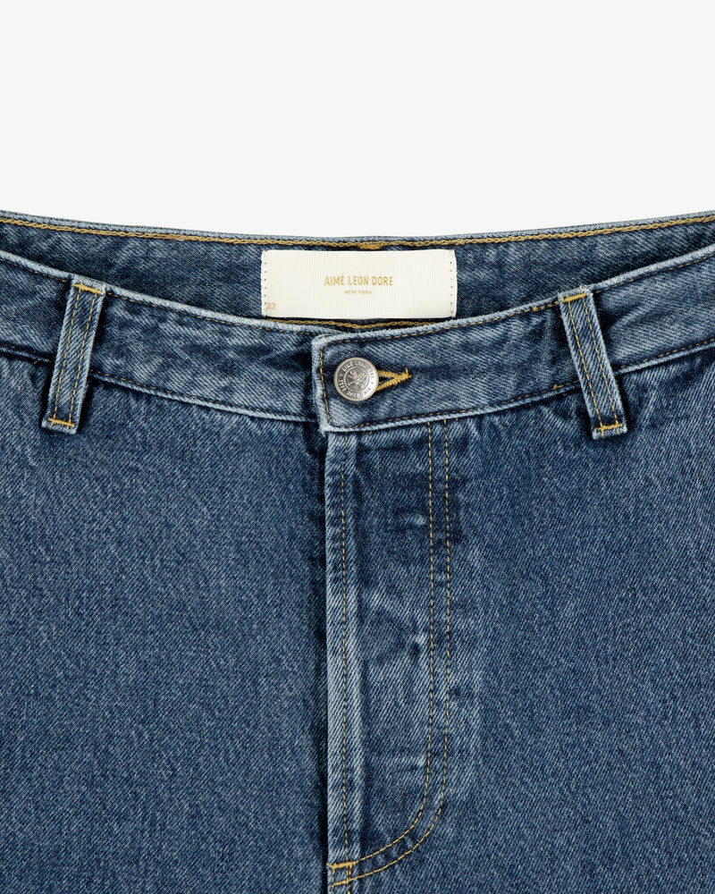 Close-up of Denim Carpenter Pant with button fly and white AIME LEON DORE label on the inner waistband.