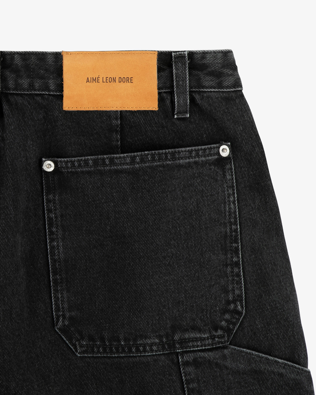 Close-up of Denim Carpenter Pant in black, showing a back pocket and tan leather AIME LEON DORE label.