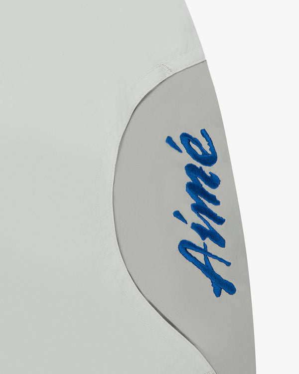 Close-up of a light gray Paneled Sport Short with Aimé stitched in blue cursive on a curved panel.