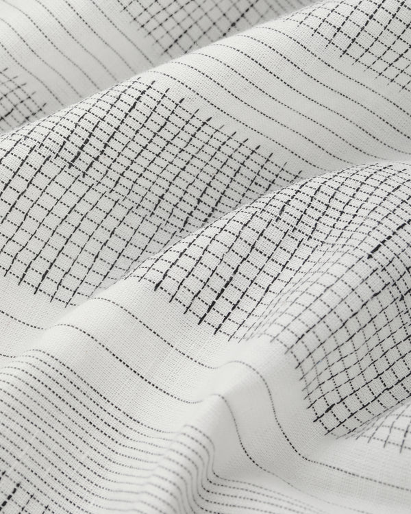 Fil Coupé Leisure Shirt in white fabric with black grid lines, softly folded to reveal texture and shadows.