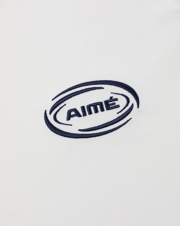 AIMÉ is embroidered in navy blue with swirling ovals on white Team Leon Performance Jersey fabric.