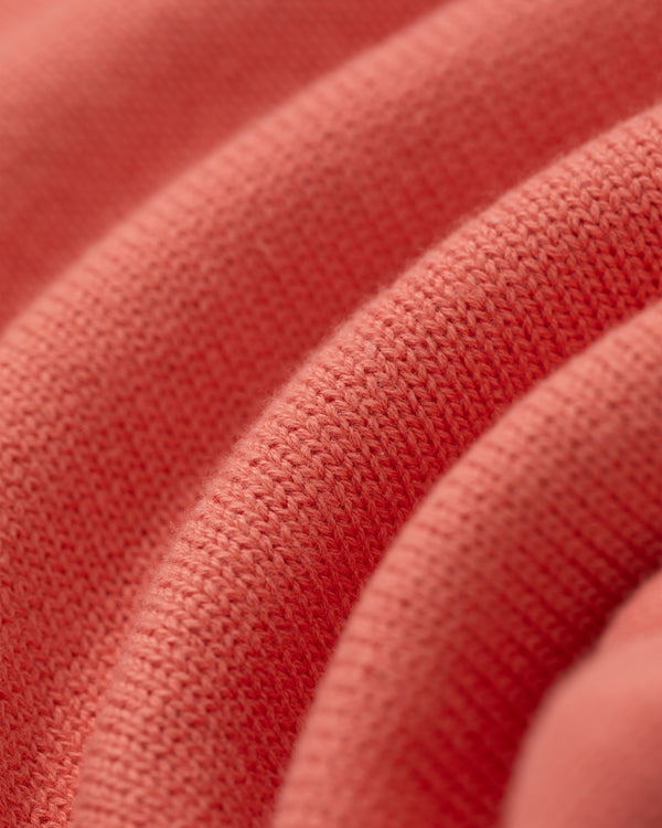 Close-up of the Heritage Mockneck Sweater’s soft, coral knit fabric with textured pattern and gentle folds.