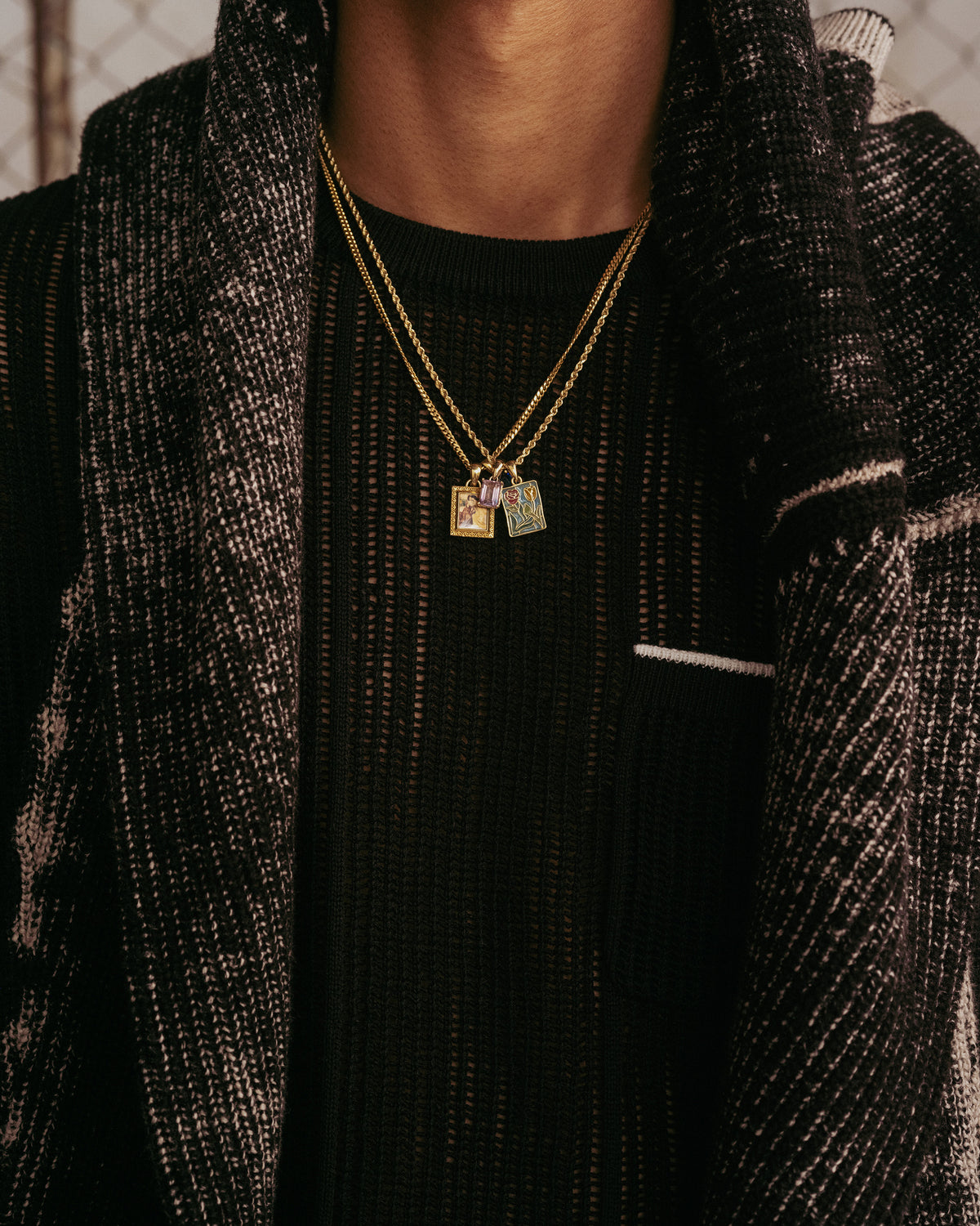 Person wearing the 14Kt Gold Stained Glass Crest Pendant over a sheer black top and black and white textured jacket.