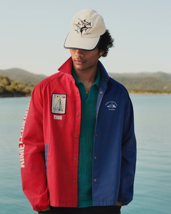 A man in a Souvenir Fishing Hat stands outdoors by water, looking down.