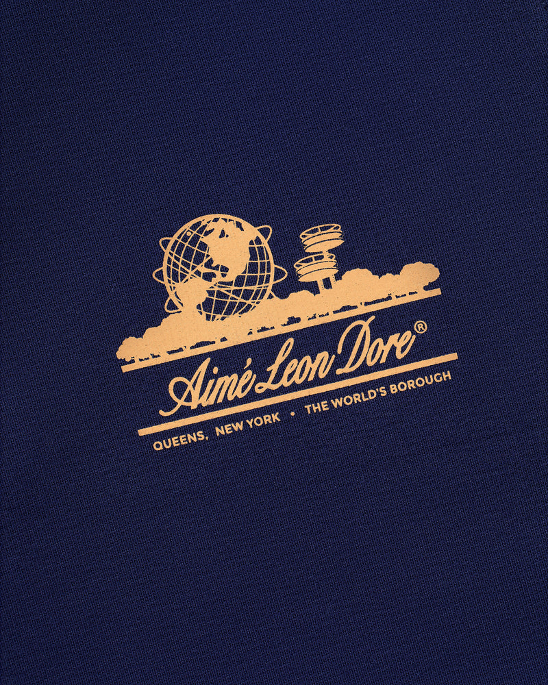 Gold Aimé Leon Dore logo featuring globe and skyline on dark blue Unisphere Sweatpants; reads Queens, New York.