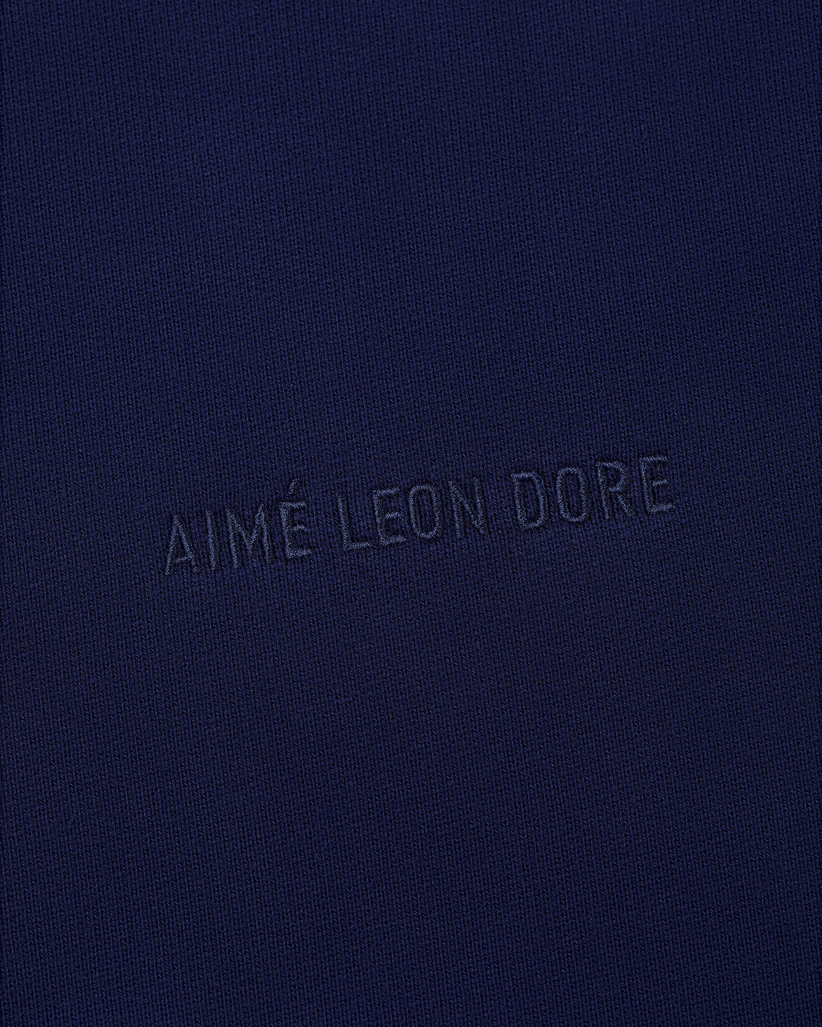 The Tonal Logo Hoodie features navy blue fabric with AIMÉ LEON DORE embossed in matching blue at the center.