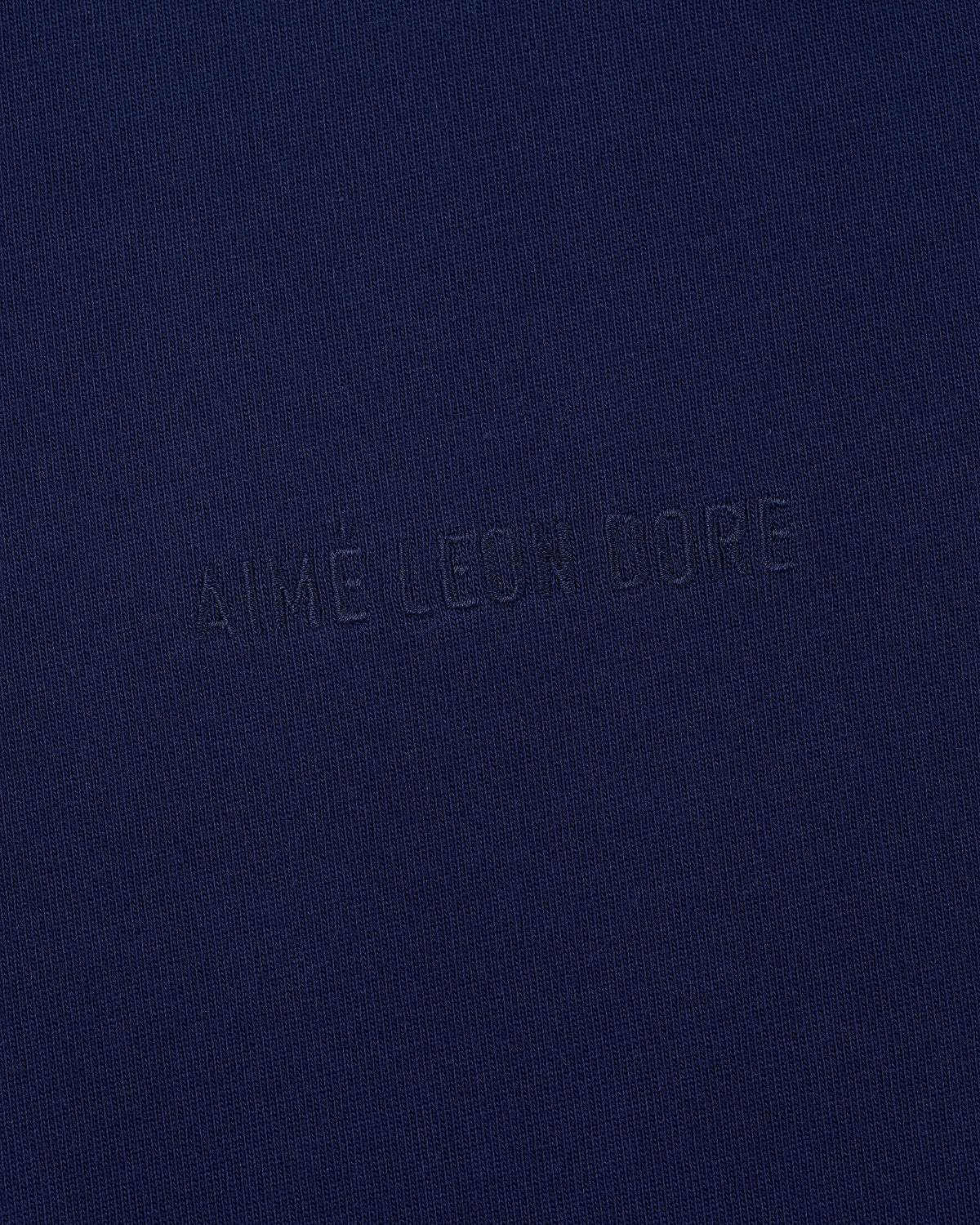 Close-up of the Tonal Logo Tee featuring AIMÉ LEON DORE subtly embroidered in matching dark blue thread.