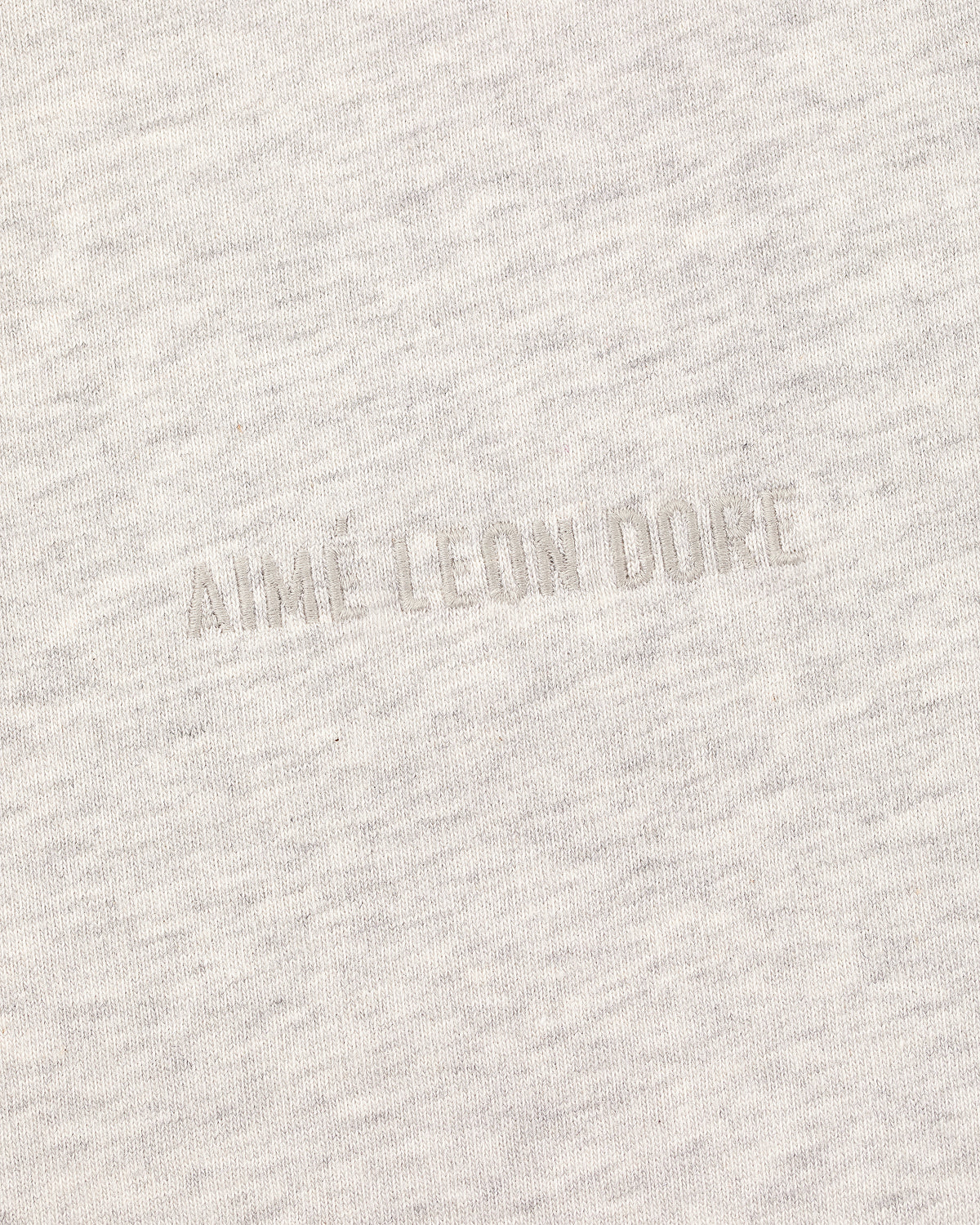 Close-up of the Tonal Logo Tee's light gray fabric with a subtle, textured tonal AIME LEON DORE embroidery.