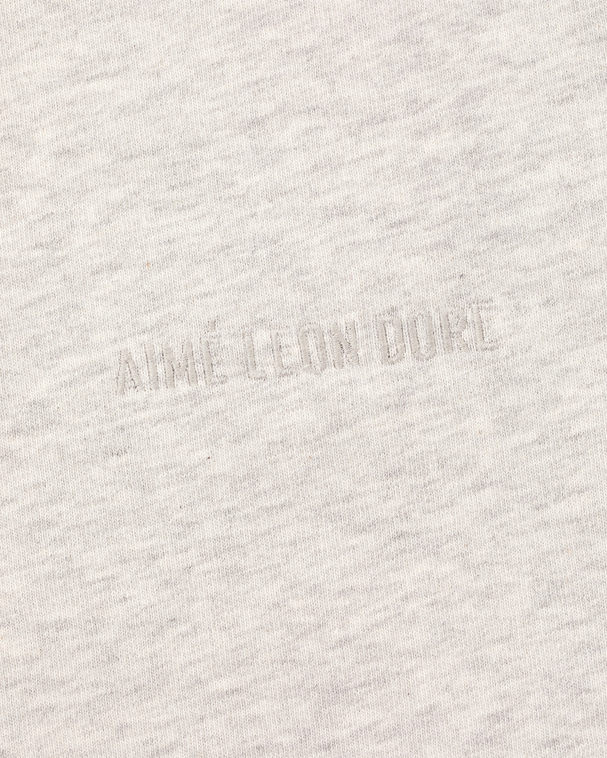 Close-up of the Long-Sleeve Tonal Logo Tee's light gray fabric with an embossed AIMÉ LEON DORE logo blending in.
