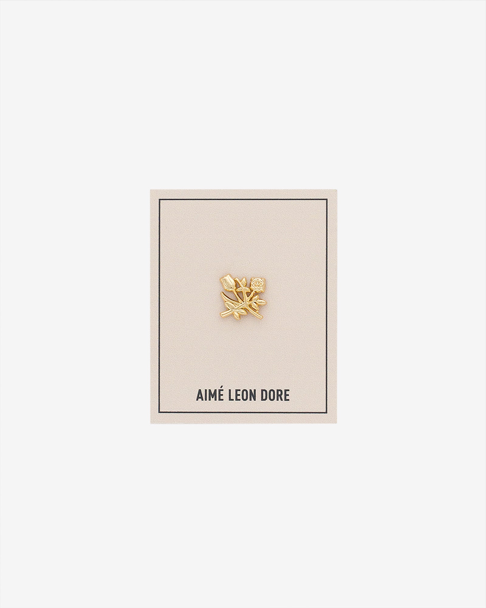 An ALD Pin shaped like a gold leaf is displayed on a beige AIMÉ LEON DORE card against a white background.
