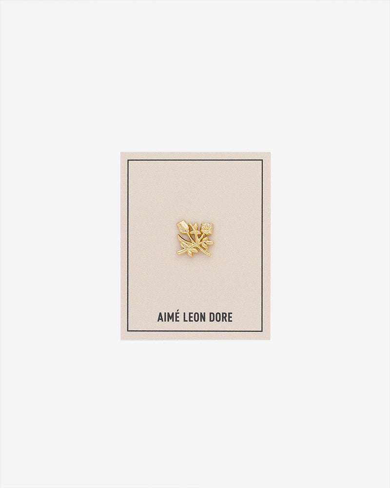 An ALD Pin shaped like a gold leaf is displayed on a beige AIMÉ LEON DORE card against a white background.