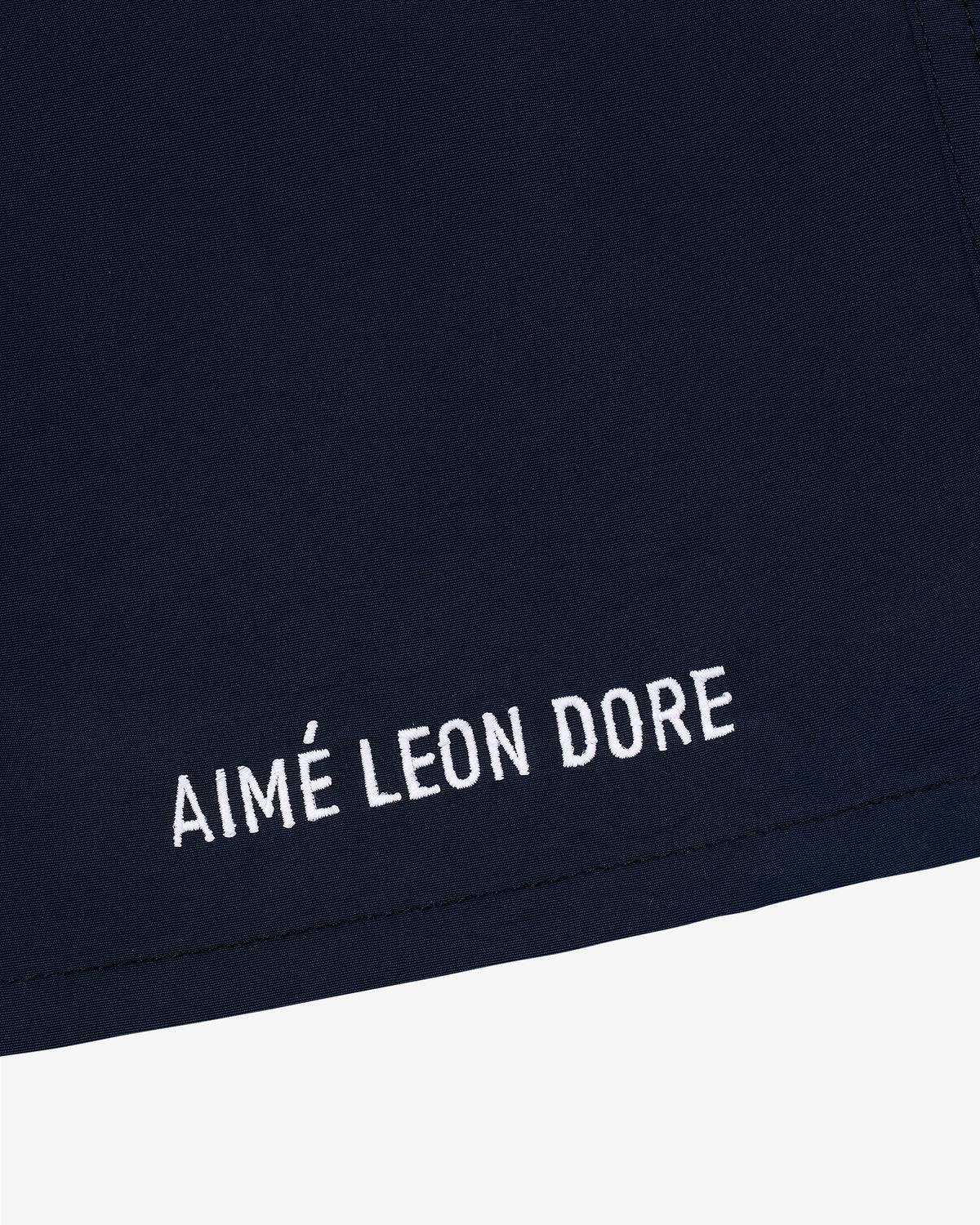 Close-up of Core Nylon Short in navy blue with AIMÉ LEON DORE embroidered in white near the hem.