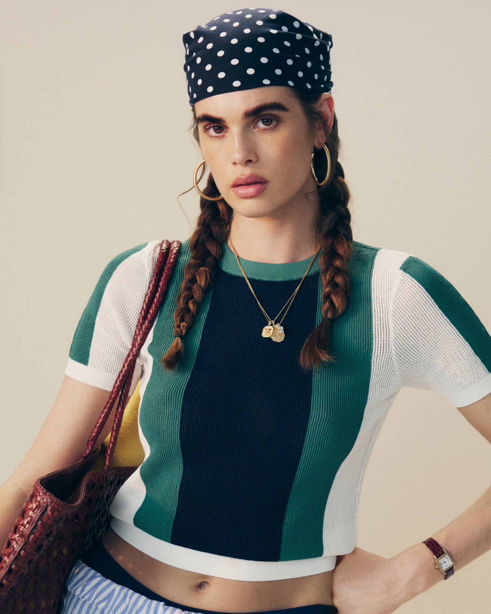 Woman with two braids in a polka-dot bandana, hoop earrings, and a Striped Mesh Knit Tee, carrying a woven bag.