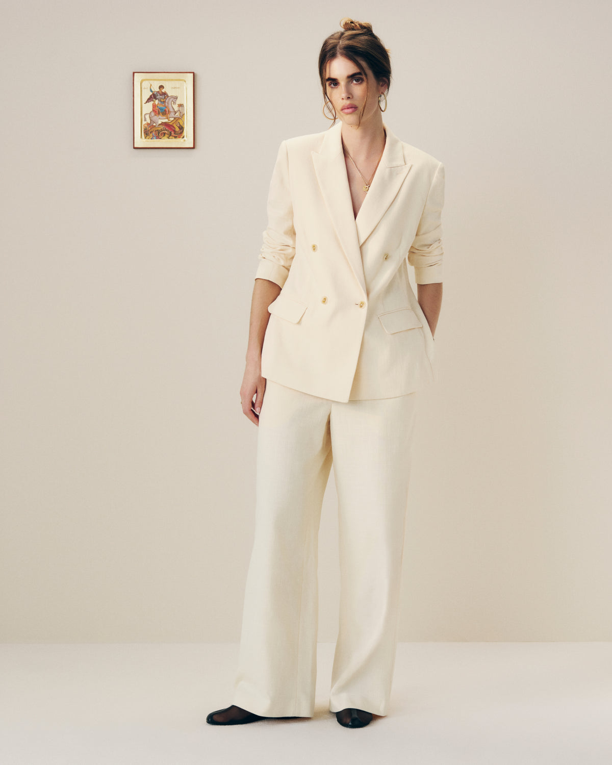 Woman wears a Double-Breasted Unconstructed Blazer indoors, hands in pockets, with framed art on the wall behind her.
