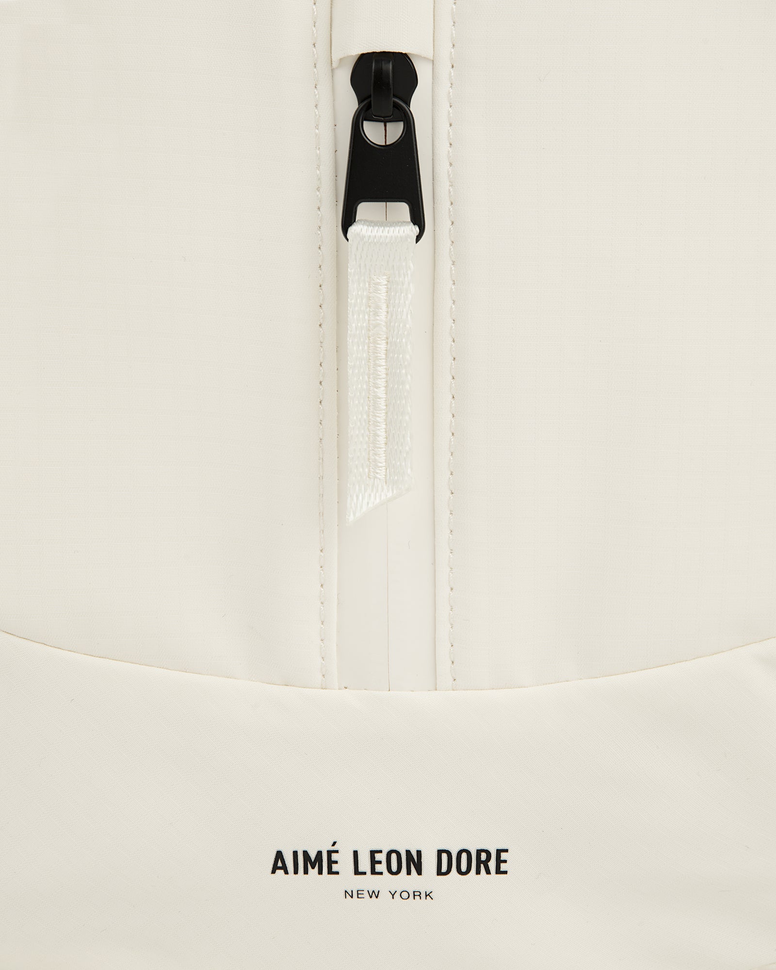 Close-up of a white Nylon Messenger Bag with a zipper and AIMÉ LEON DORE NEW YORK logo at the bottom.