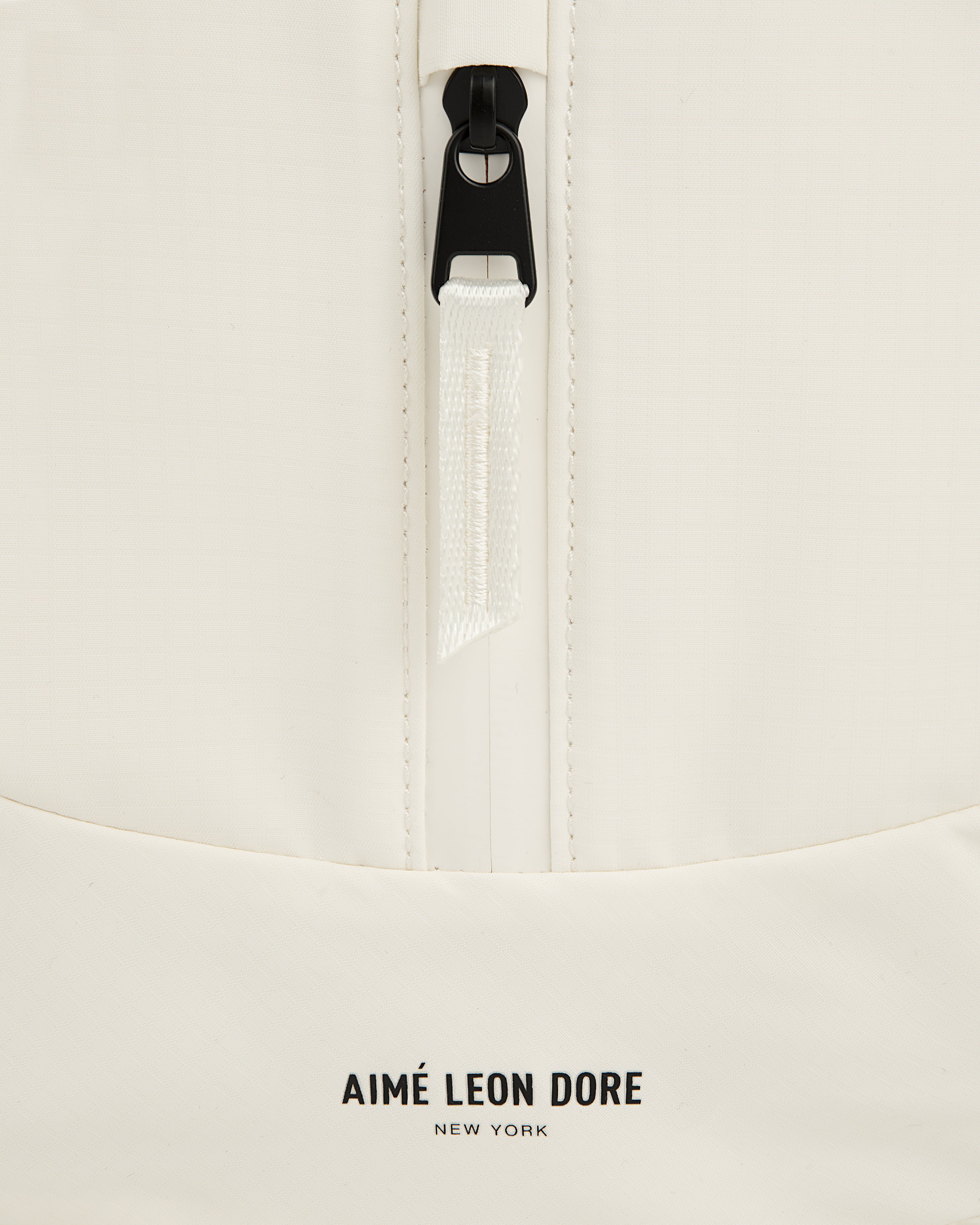 Close-up of a white Nylon Messenger Bag with a zipper and AIMÉ LEON DORE NEW YORK logo at the bottom.
