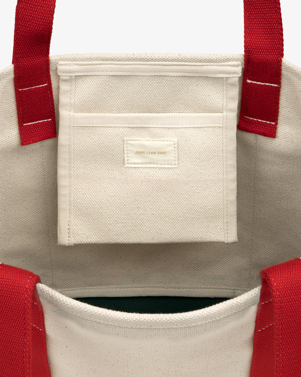 Inside view of the Small Crest Contrast Tote Bag in beige canvas with red handles and a small inner pocket.