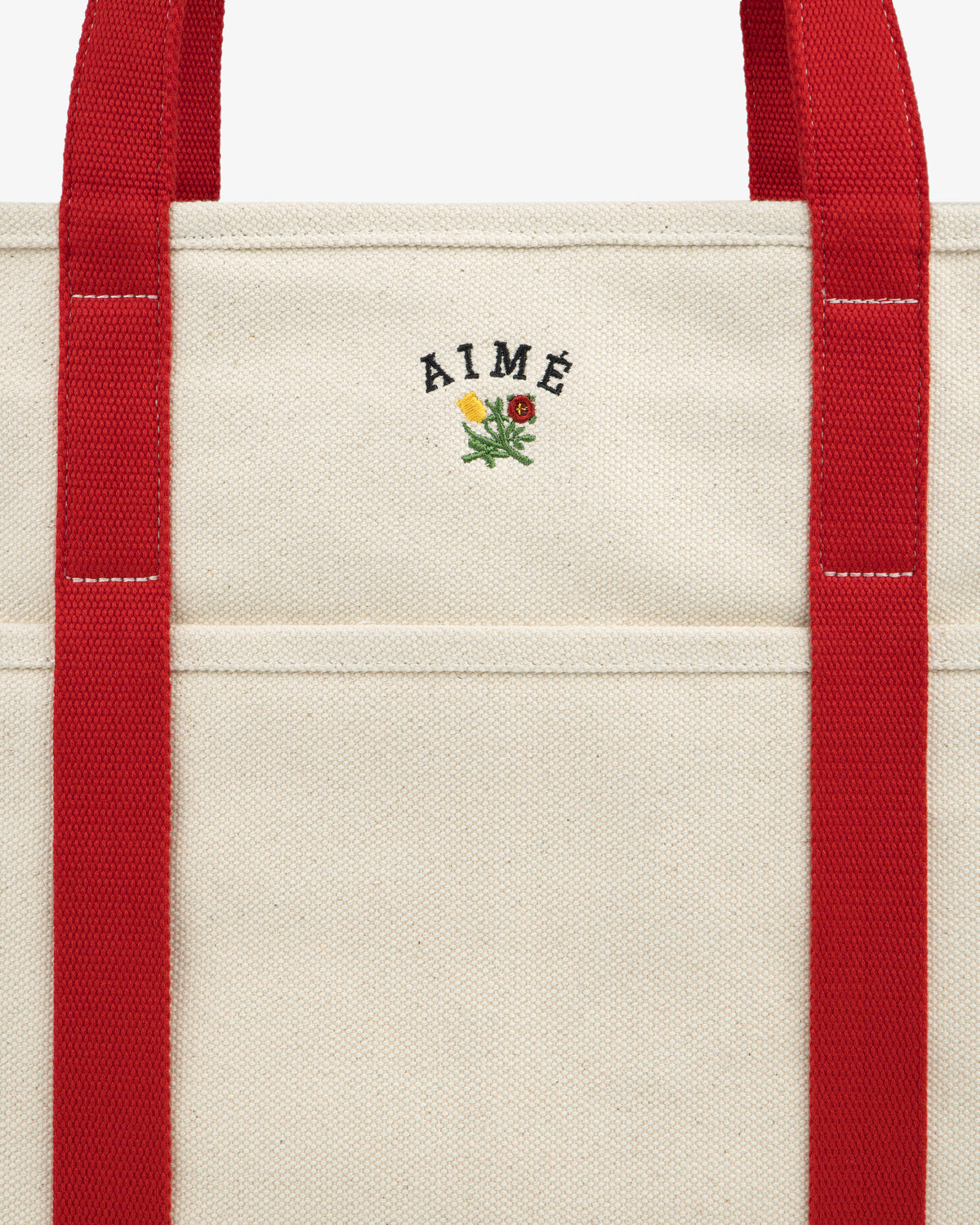 Large Crest Contrast Tote Bag in beige with red straps, AIMÉ text, and a small yellow and red flower embroidery.