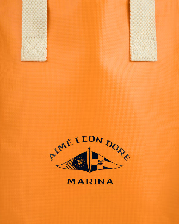 Marina Bottle Tote: Orange bag with cream handles, AIMÉ LEON DORE MARINA and two black nautical flags printed.