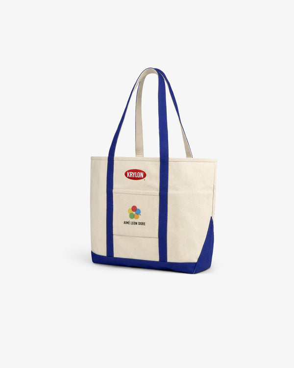 Krylon Tote Bag: Beige canvas tote with blue straps and colorful Aimé Leon Dore graphic on the front.