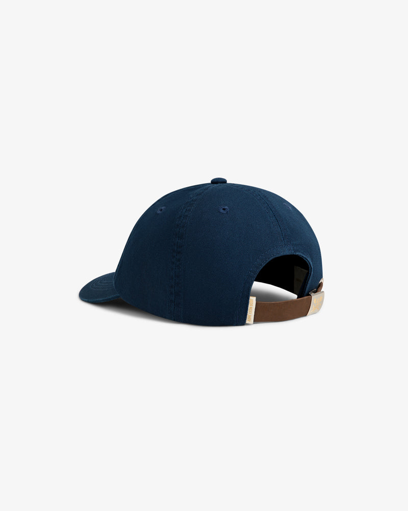 The Crest Logo Hat is a navy blue baseball cap with a brown adjustable strap and metal buckle, shown on white.