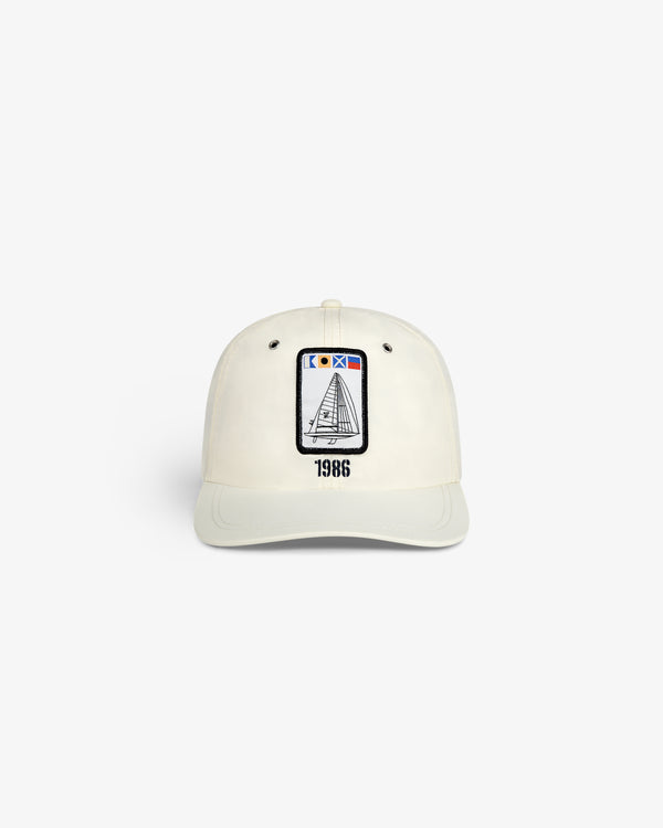 The Nylon Deck Hat is a white baseball cap with an embroidered sailboat patch and "1986" printed below it on the front.