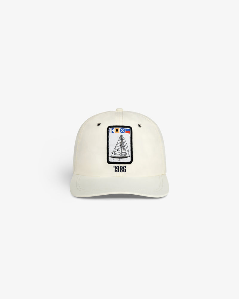 The Nylon Deck Hat is a white baseball cap with an embroidered sailboat patch and "1986" printed below it on the front.