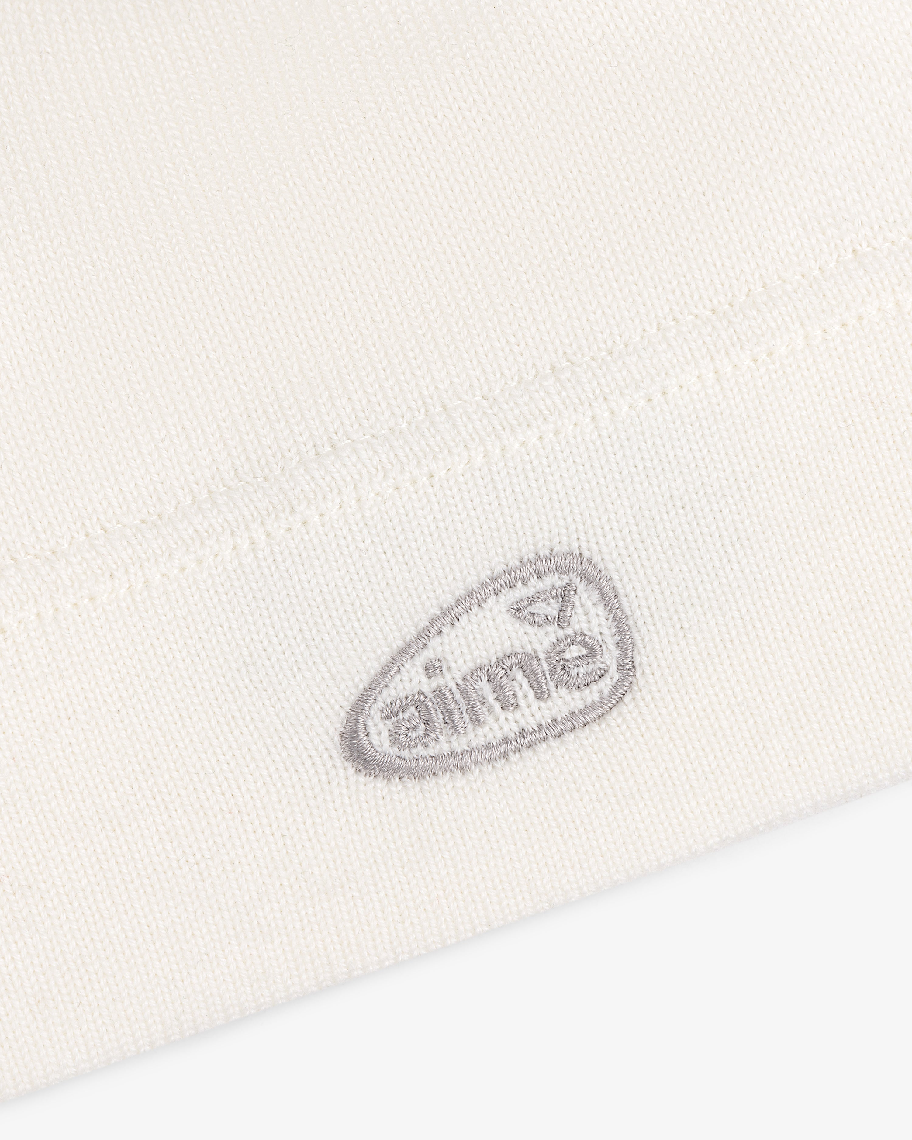 Close-up of the ALD Golf Skull Cap's white knit fabric with a small gray aimé logo embroidered near the hem.