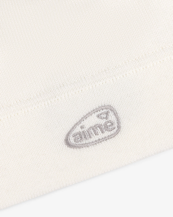 Close-up of the ALD Golf Skull Cap's white knit fabric with a small gray aimé logo embroidered near the hem.
