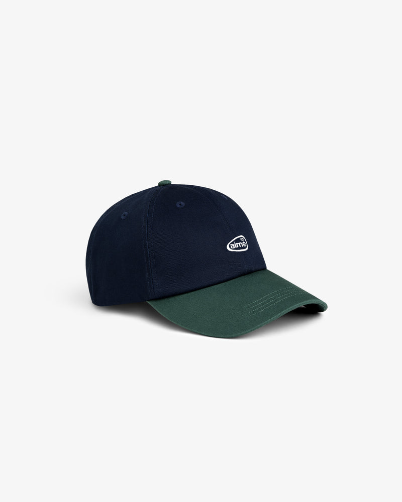 The ALD Golf Logo Hat is a two-tone cap with a navy crown, dark green brim, and small white logo on the front.