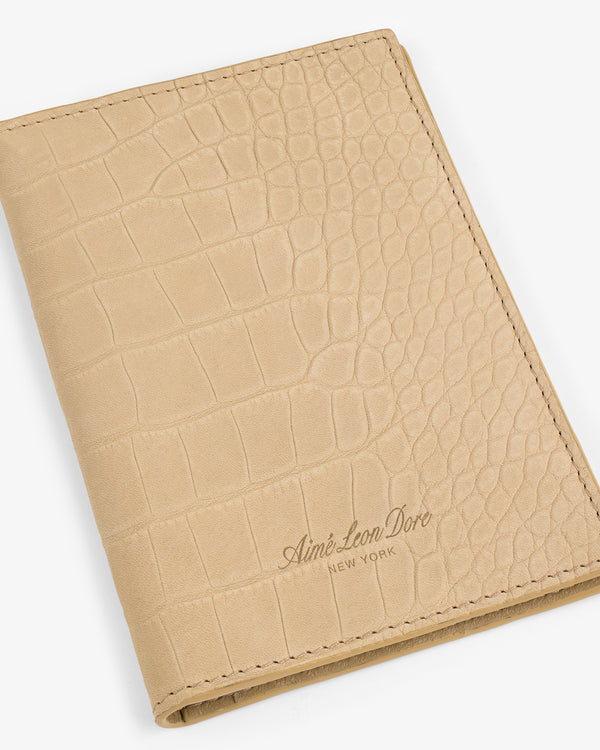 Beige croc-embossed nubuck passport holder with Aimé Leon Dore New York embossed on the lower right corner.