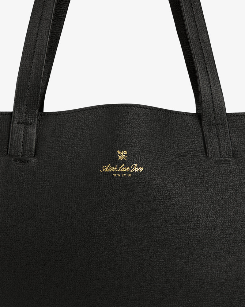 Close-up of a Full Grain Leather Tote Bag in black with Aimé Leon Dore New York and gold crest logo on the front.