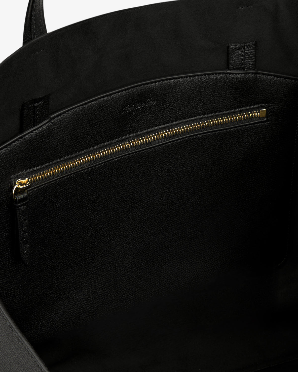 Close-up of the Full Grain Leather Tote Bag's black leather interior with gold zipper pocket and suede lining.