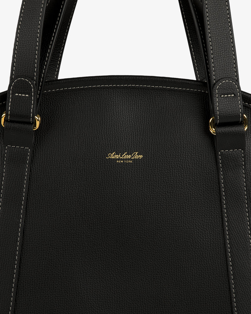 Close-up of the Full Grain Leather Weekender Bag, black with white stitching, gold hardware, and a central gold logo.