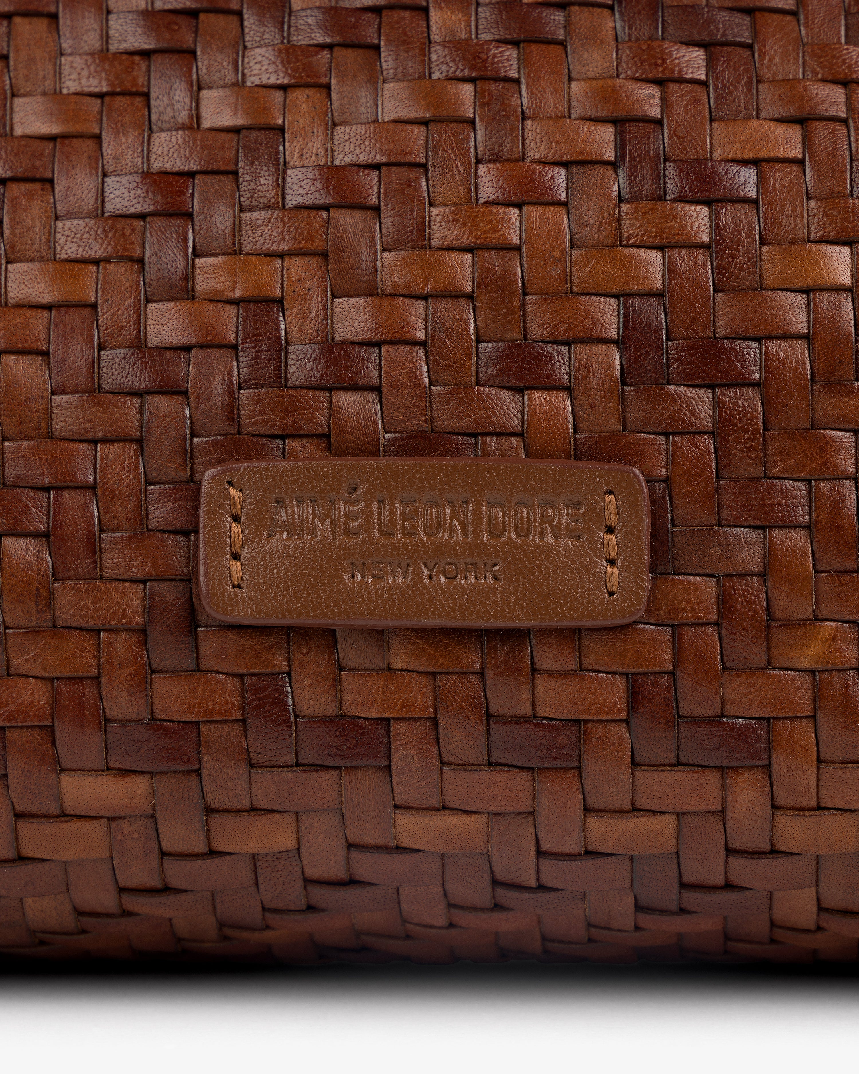 Close-up of the Woven Leather Shoulder Bag’s brown weave and stitched AIMÉ LEON DORE NEW YORK label.
