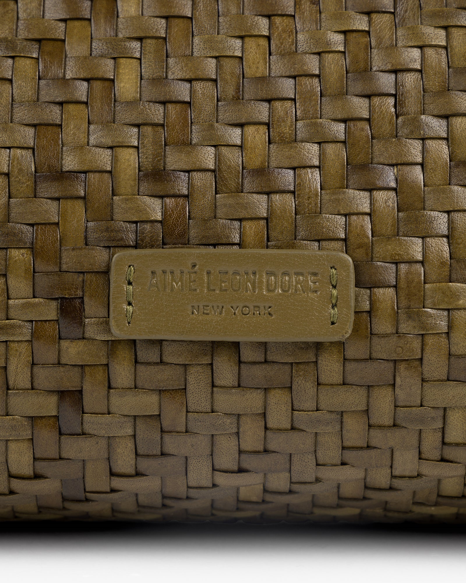 Close-up of a Woven Leather Shoulder Bag with an Aimé Leon Dore New York label stitched at the center.
