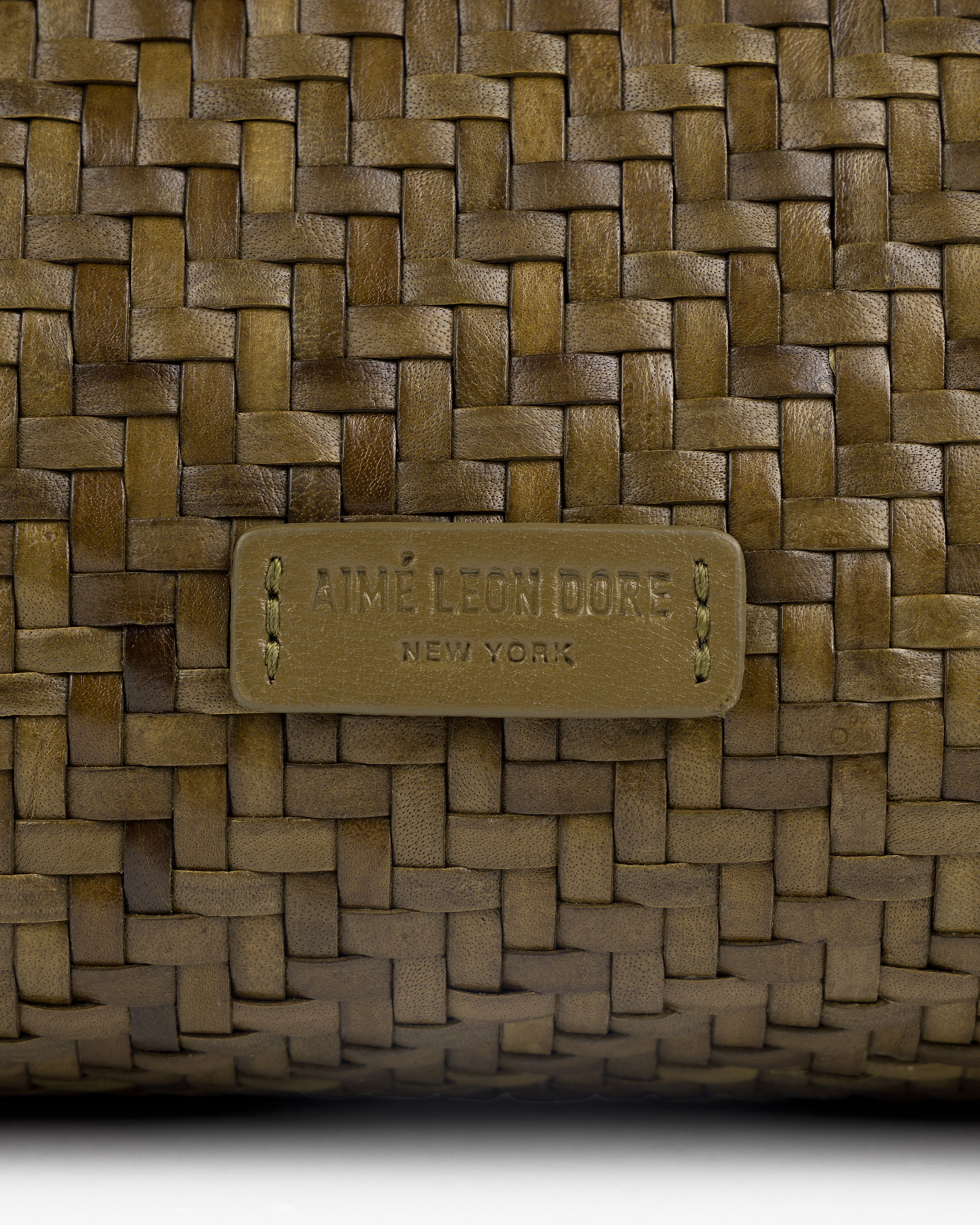 Close-up of a Woven Leather Shoulder Bag with an Aimé Leon Dore New York label stitched at the center.