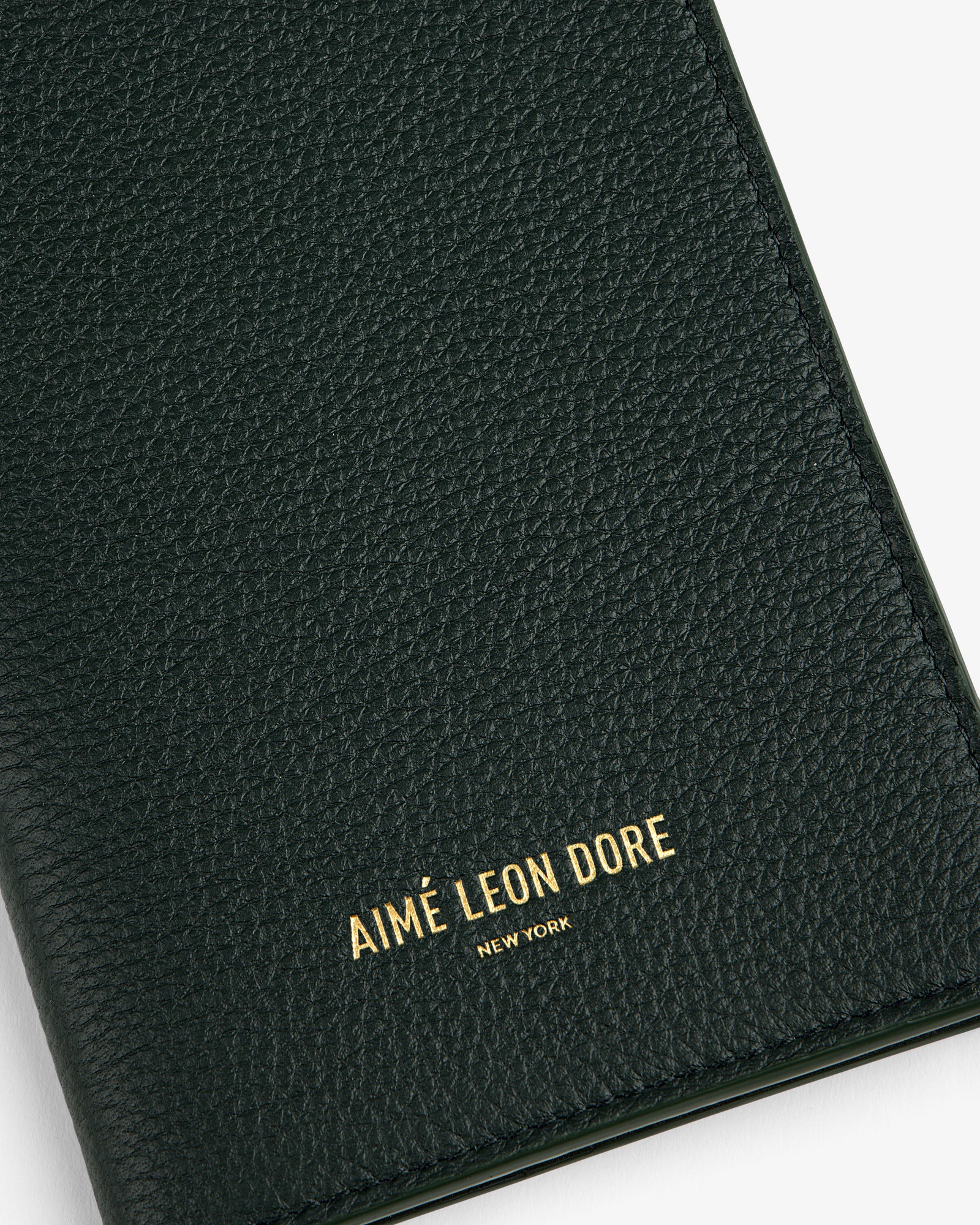 Close-up of a textured dark green Leather Passport Holder with AIMÉ LEON DORE NEW YORK in gold lettering.