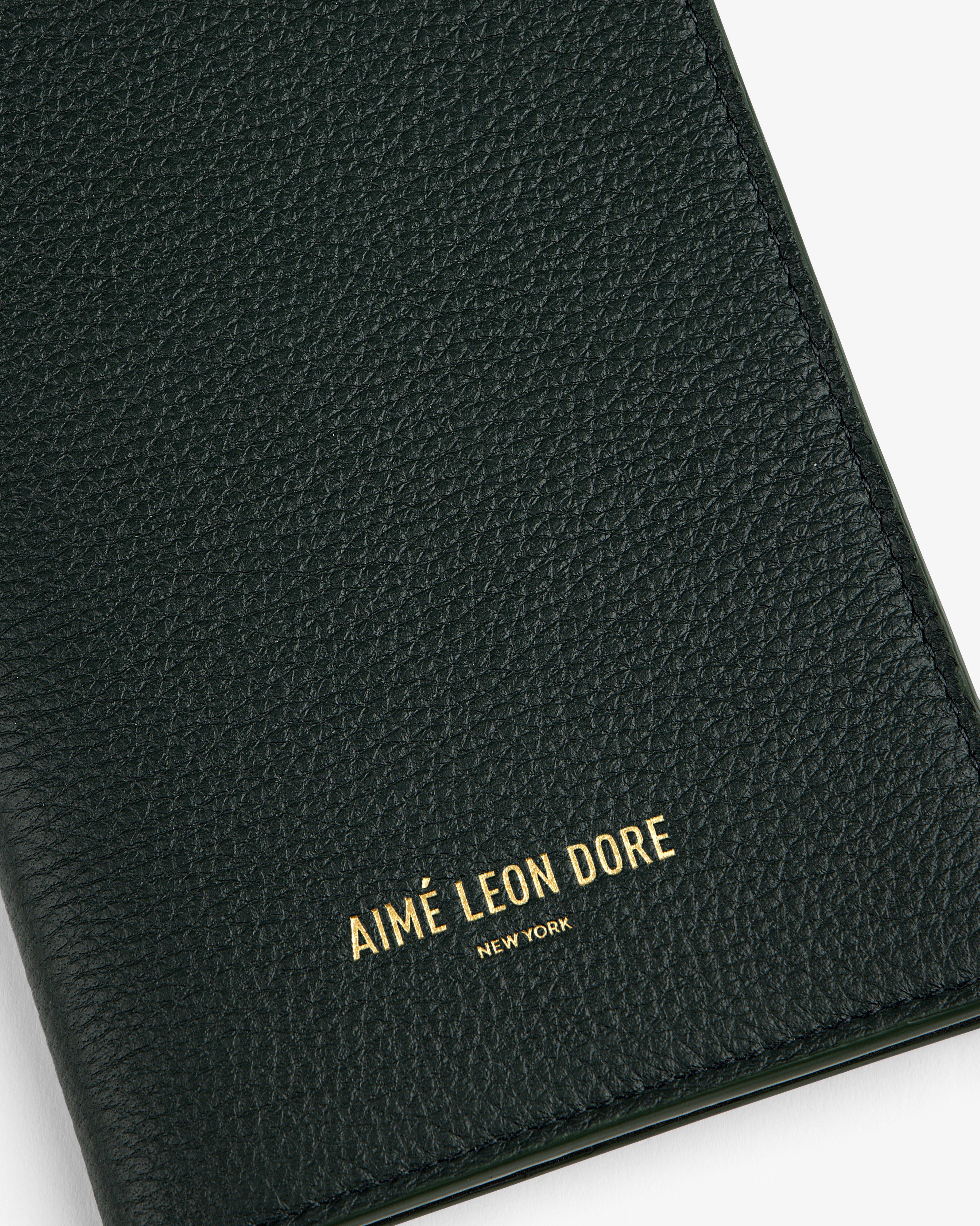 Close-up of a textured dark green Leather Passport Holder with AIMÉ LEON DORE NEW YORK in gold lettering.