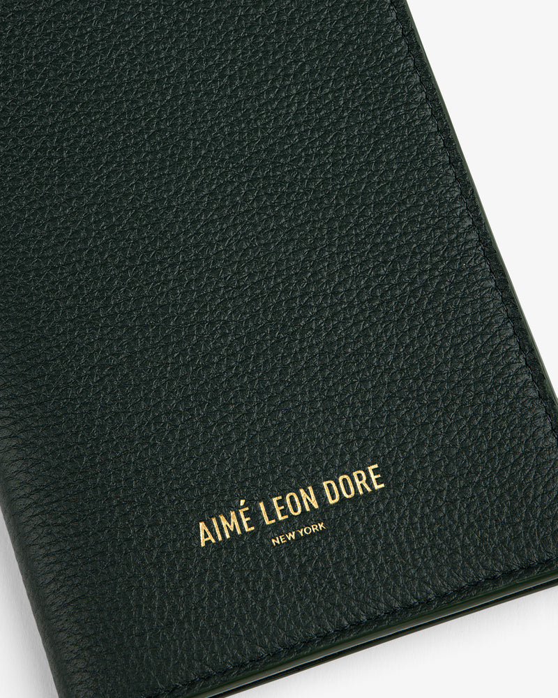 Close-up of a textured dark green Leather Passport Holder with AIMÉ LEON DORE NEW YORK in gold lettering.