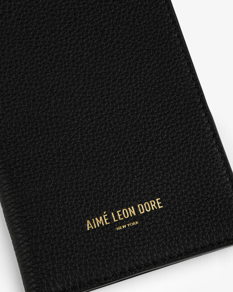 Black textured leather passport holder with AIMÉ LEON DORE NEW YORK embossed in gold letters on the front.