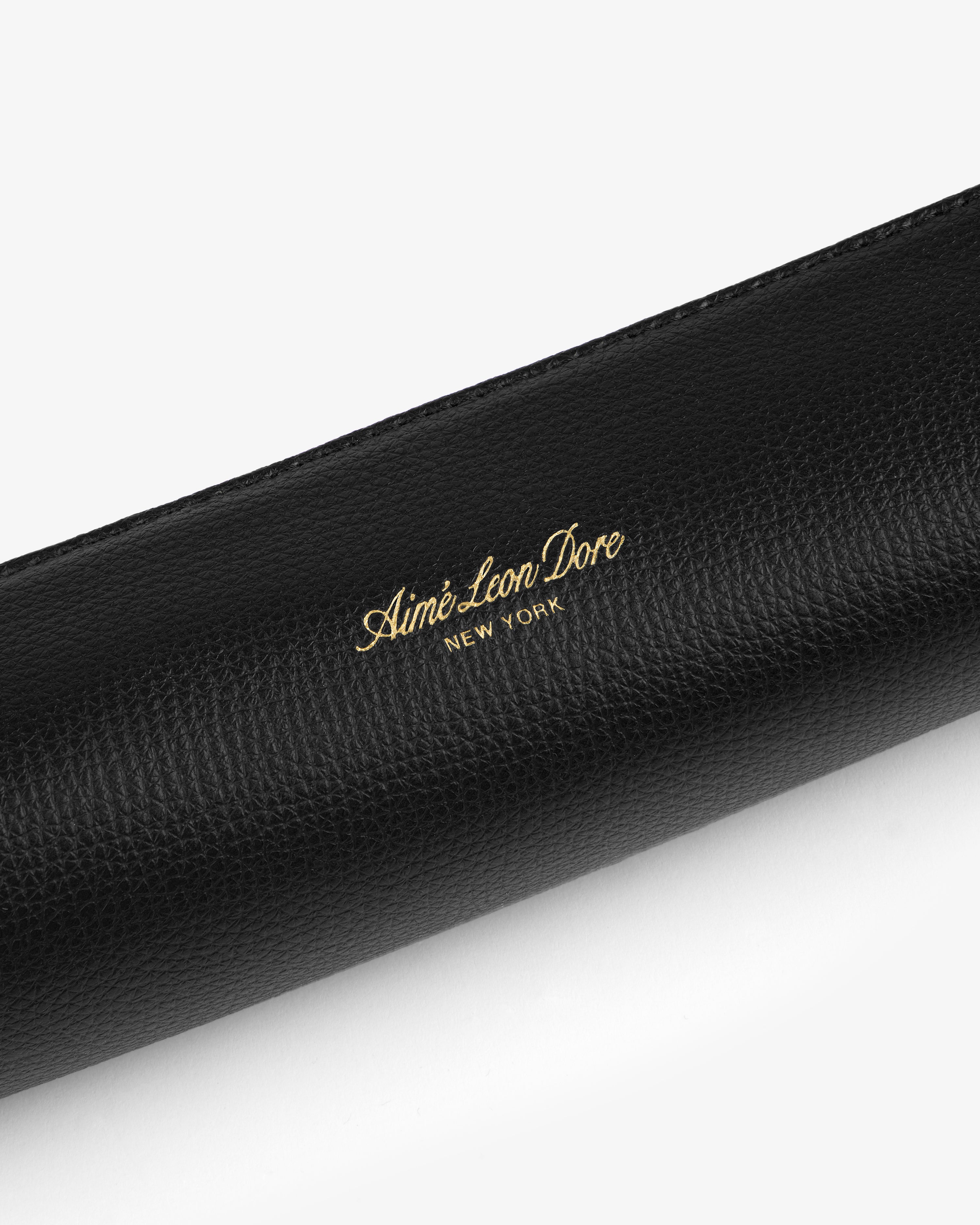 Black textured leather pencil case with gold Aimé Leon Dore New York logo embossed at the center.