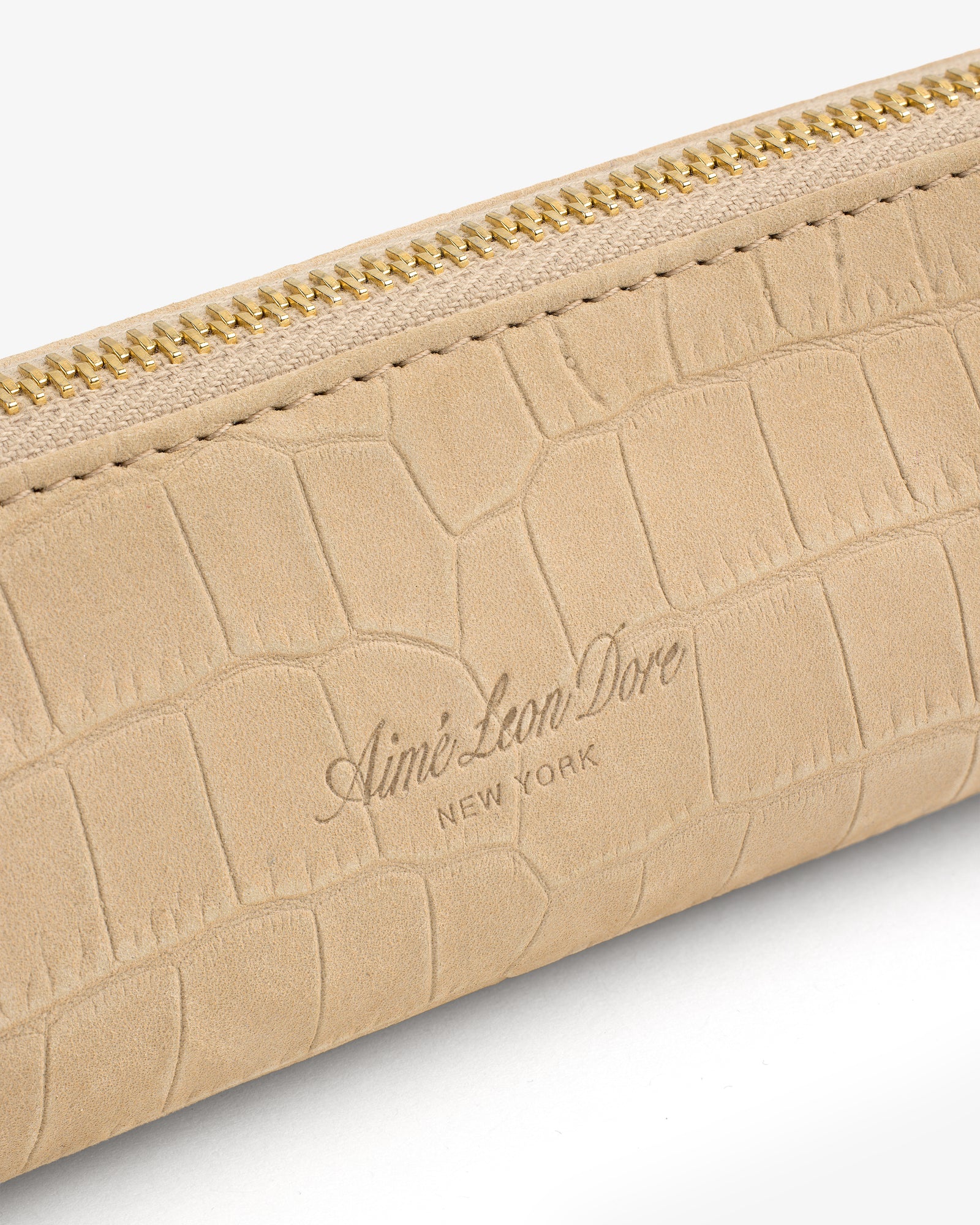 Close-up of the Croc-Embossed Nubuck Pencil Case with gold zipper and Aimé Leon Dore New York embossed on beige leather.