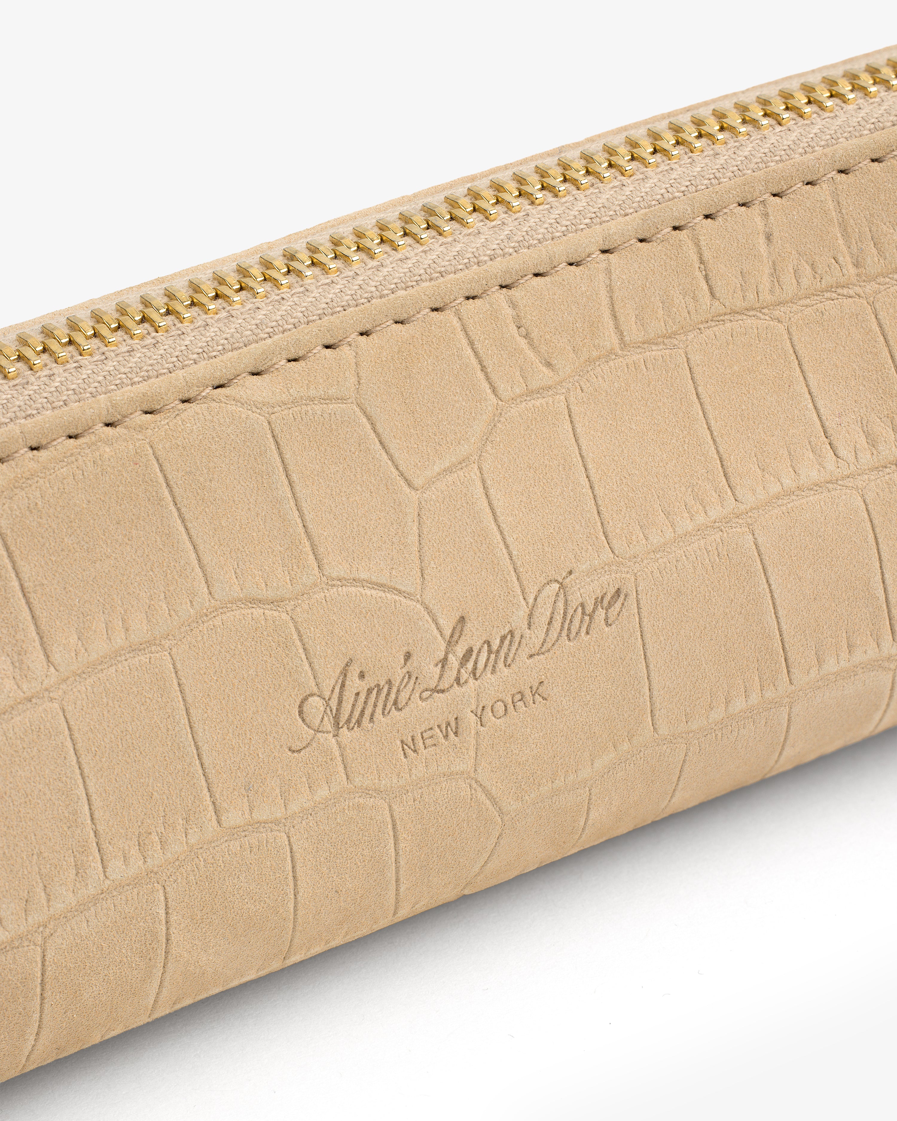 Close-up of the Croc-Embossed Nubuck Pencil Case with gold zipper and Aimé Leon Dore New York embossed on beige leather.
