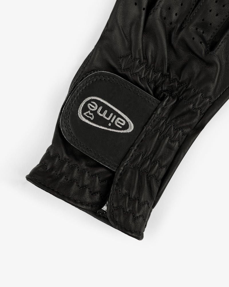 A close-up of the ALD / FootJoy StaSof Heritage Glove (Right) in black leather with a velcro strap labeled "aimé.